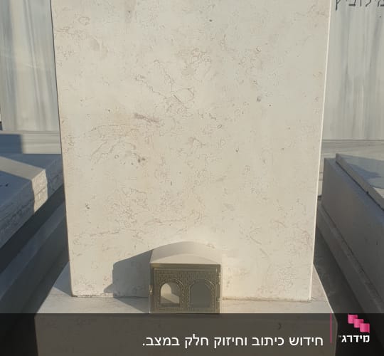 מצבה עם כיתוב בעברית וחפץ מתכת קטן